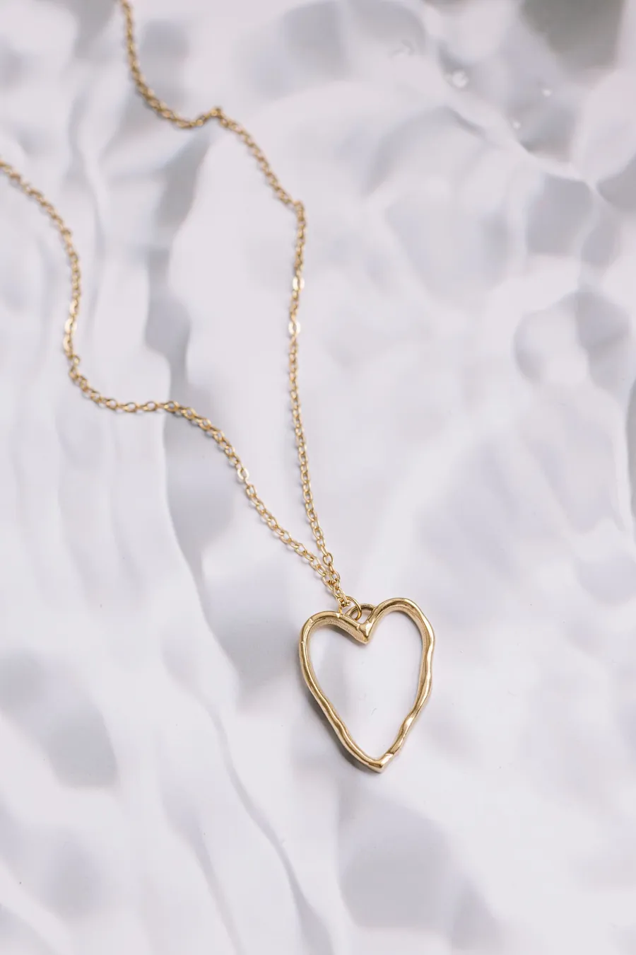 Collar fino de oro con dije de corazón calado sobre tela blanca